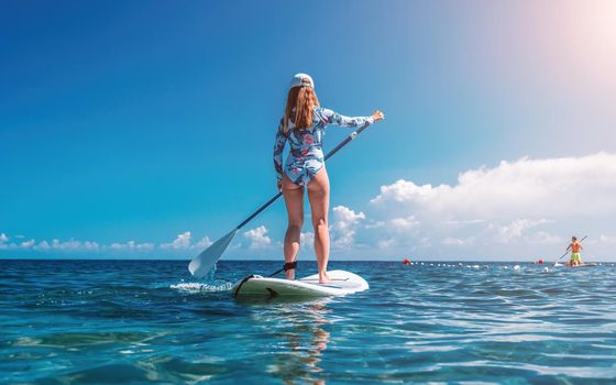 SUP Stand up paddle board. Young woman sailing on beautiful calm sea with crystal clear water. The concept of an summer holidays vacation travel, relax, active and healthy life in harmony with nature