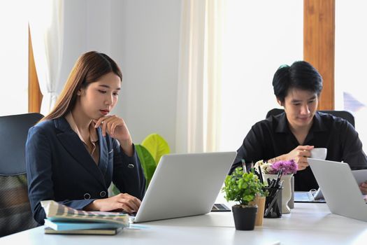 Concentrated businesswoman and young businessman using laptop computers at coworking space.