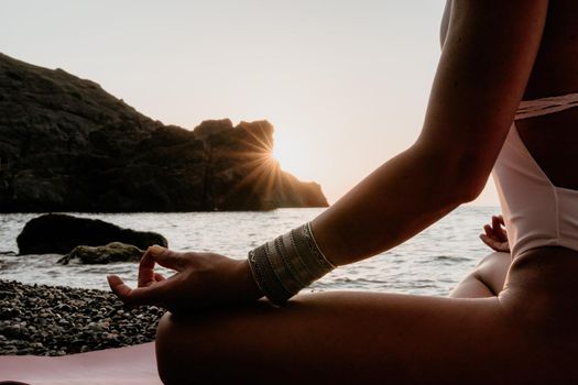 Young woman in swimsuit with long hair practicing stretching outdoors on yoga mat by the sea on a sunny day. Women's yoga fitness pilates routine. Healthy lifestyle, harmony and meditation concept.