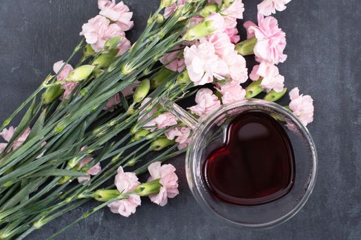 pink carnations on a dark background with a cup of red tea in a heart-shaped cup, valentine's day, mother's day, gifts for loved ones. High quality photo