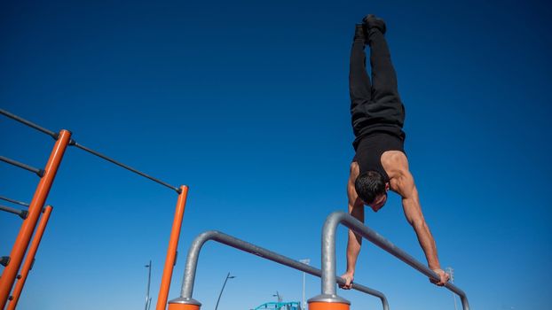 Shirtless man doing handstand on parallel bars at sports ground