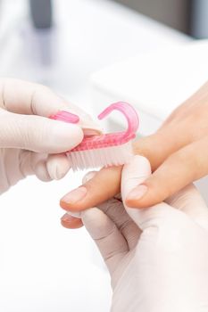 Close up of manicure master in white gloves uses brush to clean dust from female nails in beauty salon