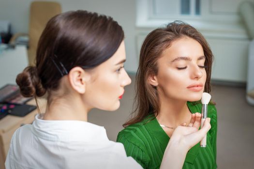 Make up artist applying professional make up of tonal foundation on the face of beautiful young caucasian woman in make up room. Base for make up.