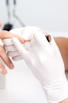 Manicure master in protective gloves applying beige nail polish on female nails in beauty salon