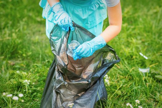 Child collects plastic trash from grass throwing garbage in garbage bag in the park