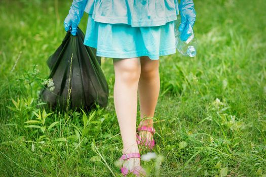 Little girl with crumpled plastic bottle and garbage bag in her hands while cleaning garbage in the park