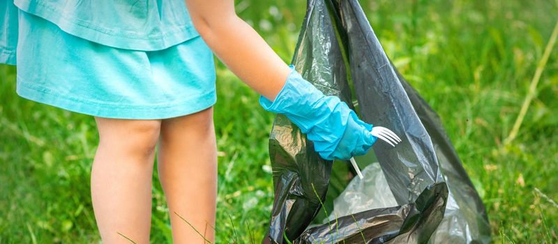 Child collects plastic trash from grass throwing garbage in garbage bag in the park