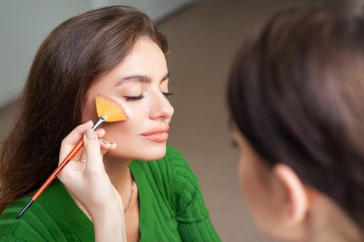 Make up artist applying professional make up of tonal foundation on the face of beautiful young caucasian woman in make up room. Base for make up.