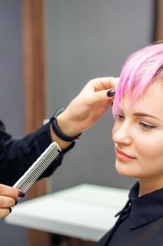 Young woman receiving short pink hairstyle by female hairdresser in beauty salon