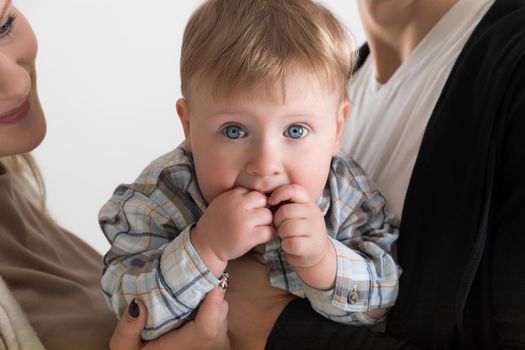 Close-up portrait of a happy one-year-old baby in the arms of his parents.