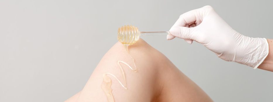 Wax on honey stick flowing down on female leg in human hand wearing protective glove on white background