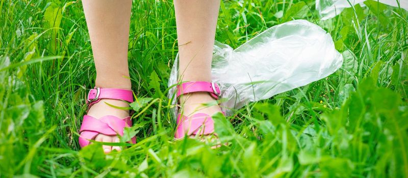 plastic bags trash with children's feet on green grass while cleaning the park from plastic debris