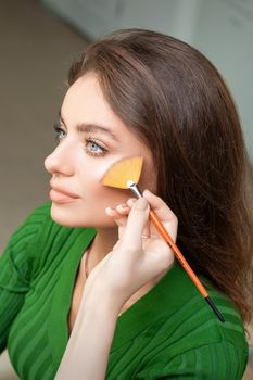 Make up artist applying professional make up of tonal foundation on the face of beautiful young caucasian woman in make up room. Base for make up.