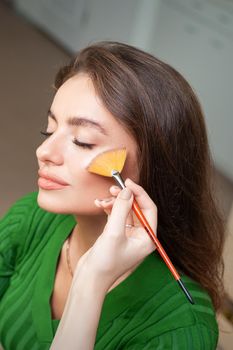 Make up artist applying professional make up of tonal foundation on the face of beautiful young caucasian woman in make up room. Base for make up.