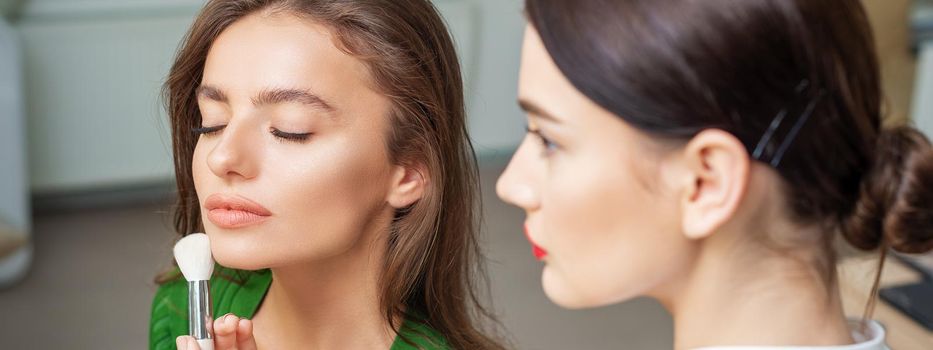 Make up artist applying professional make up of tonal foundation on the face of beautiful young caucasian woman in make up room. Base for make up.