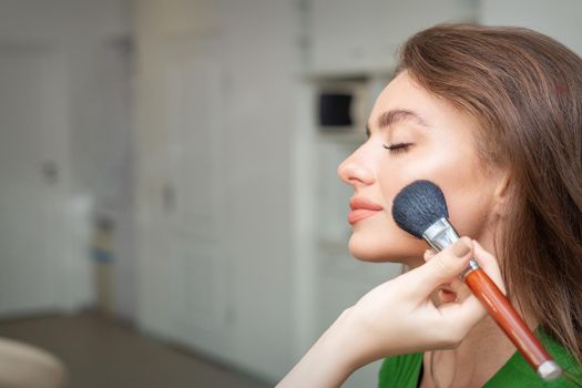 Make up artist applying professional make up of tonal foundation on the face of beautiful young caucasian woman in make up room. Base for make up.