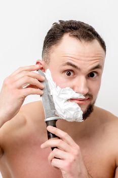 Young caucasian man shaving beard with knife on white background