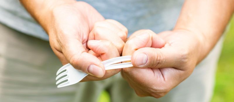 Male hand breaks plastic disposable fork in the park. The concept of environmental problems. Plastic free