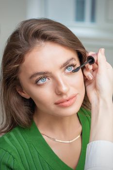 Professional makeup artist applying mascara on lashes of beautiful young caucasian woman in beauty salon