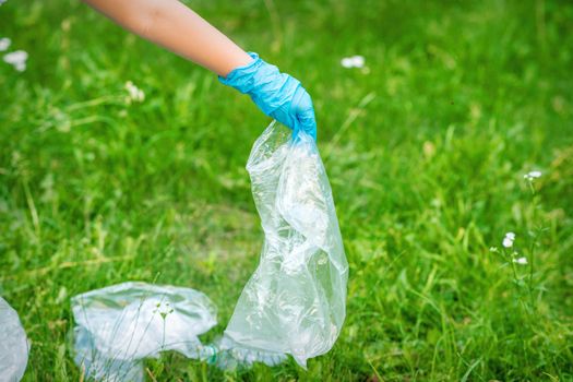 Hand of child cleans the park from plastic debris lying on the green grass