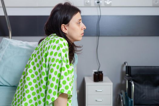 Hospitalized sick woman sitting in bed during medical consultation waiting for physician doctor in hospital ward. Stressed patient recovering after surgery