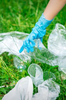 Hand of child cleans the park from plastic debris lying on the green grass