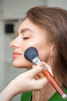 Make up artist applying professional make up of tonal foundation on the face of beautiful young caucasian woman in make up room. Base for make up.