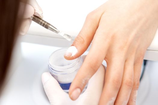 Close up of the process of applying acrylic powder on the nails of a young woman in a beauty salon