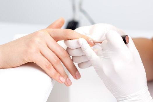 Manicure master in protective gloves applying beige nail polish on female nails in beauty salon