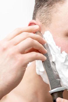 Young caucasian man shaving beard with knife on white background