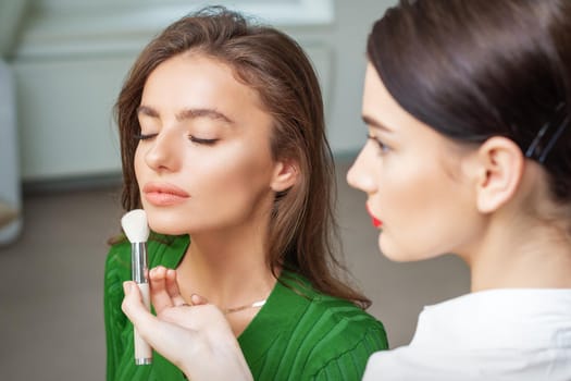 Make up artist applying professional make up of tonal foundation on the face of beautiful young caucasian woman in make up room. Base for make up.