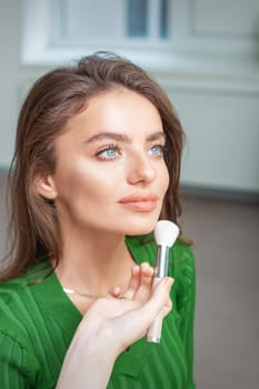 Make up artist applying professional make up of tonal foundation on the face of beautiful young caucasian woman in make up room. Base for make up.