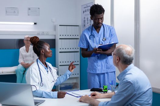 African american healthcare hospital staff reviewing senior patient record file while talking about treatment schedule. Clinic expert discussing with nurse about consultation appointments