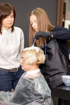 Young female trainee learns to draw women's hair under the supervision of a professional hairdresser in a barbershop