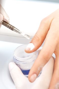 Close up of the process of applying acrylic powder on the nails of a young woman in a beauty salon