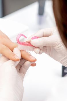 Close up of manicure master in white gloves uses brush to clean dust from female nails in beauty salon