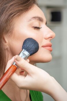 Make up artist applying professional make up of tonal foundation on the face of beautiful young caucasian woman in make up room. Base for make up.