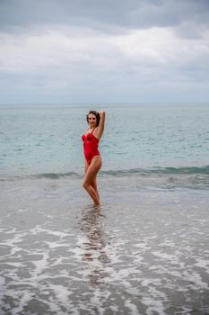 A beautiful and sexy brunette in a red swimsuit on a pebble beach, Running along the shore in the foam of the waves.