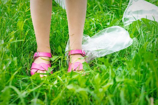 Plastic bags trash with children's feet on green grass while cleaning the park from plastic debris