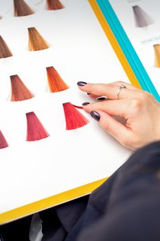 Customer's female hand choosing pink or red colour for hair colouring before hair dyeing in hair salon
