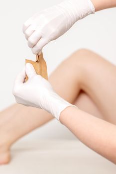 Human hands in protective gloves holding craft envelope with medical or beauty tools on background of female legs