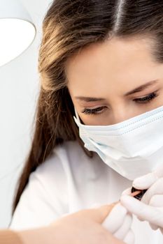 Manicure master with protective mask in rubber gloves applying beige nail polish on female nails in beauty salon