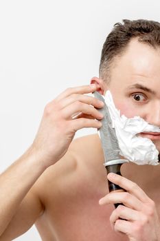 Young caucasian man shaving beard with knife on white background