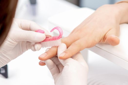 Close up of manicure master in white gloves uses brush to clean dust from female nails in beauty salon