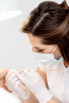 Manicure master with protective mask in rubber gloves applying beige nail polish on female nails in beauty salon