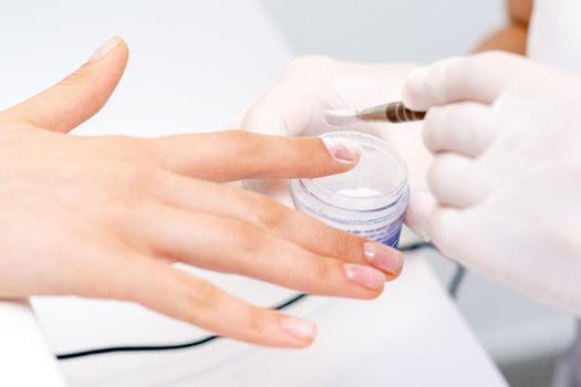 Close up of the process of applying acrylic powder on the nails of a young woman in a beauty salon