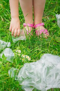 Hand of child cleans green grass from plastic trash in the park