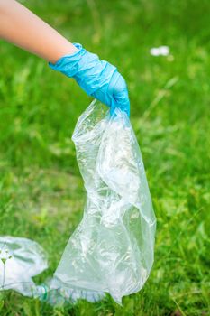 Hand of child cleans the park from plastic debris lying on the green grass