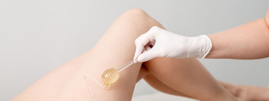 Wax on honey stick flowing down on female leg in human hand wearing protective glove on white background