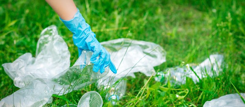 Hand of child cleans the park from plastic debris lying on the green grass